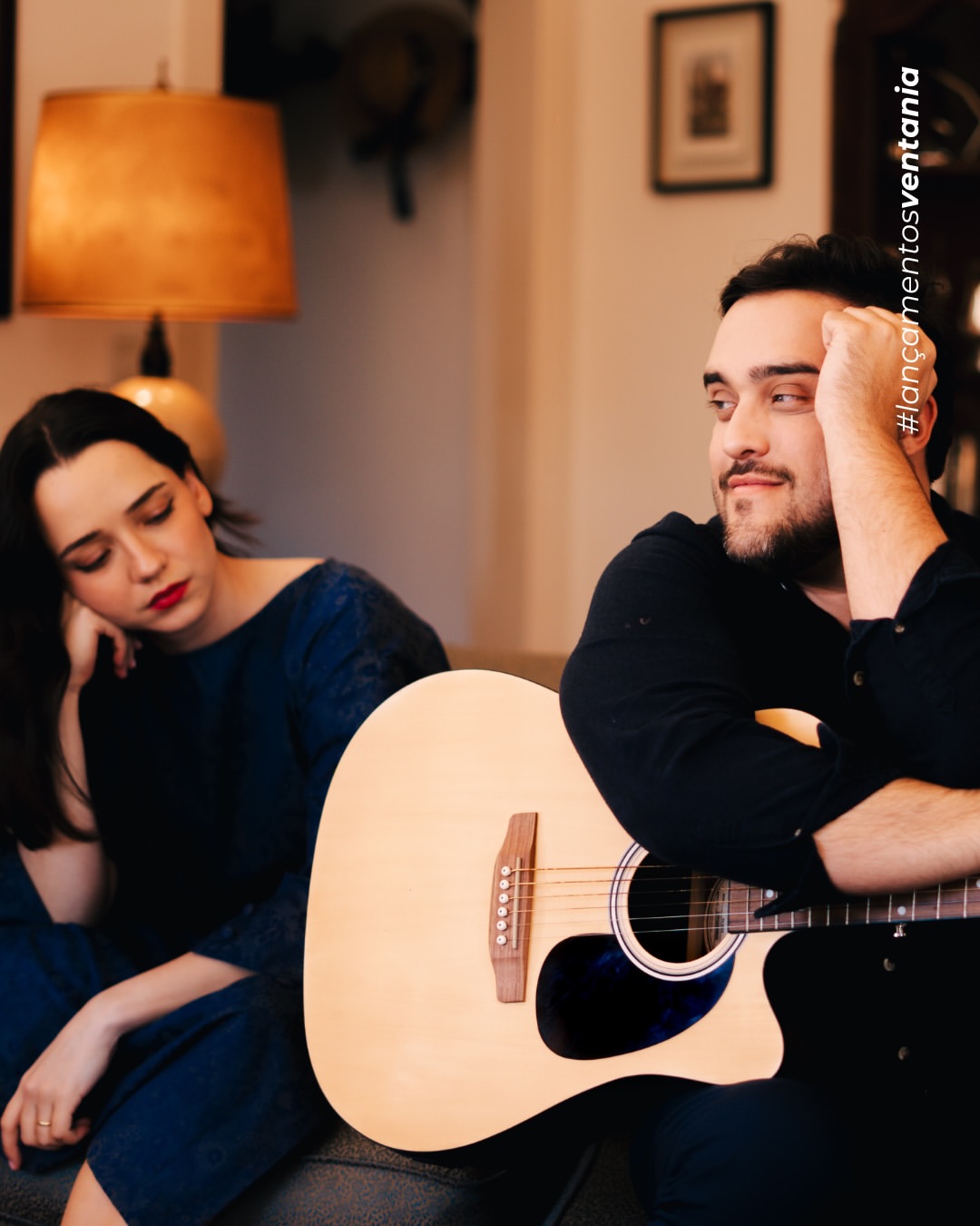 Pedro Valença e Paula Schneider numa sala de estar, com guitarra